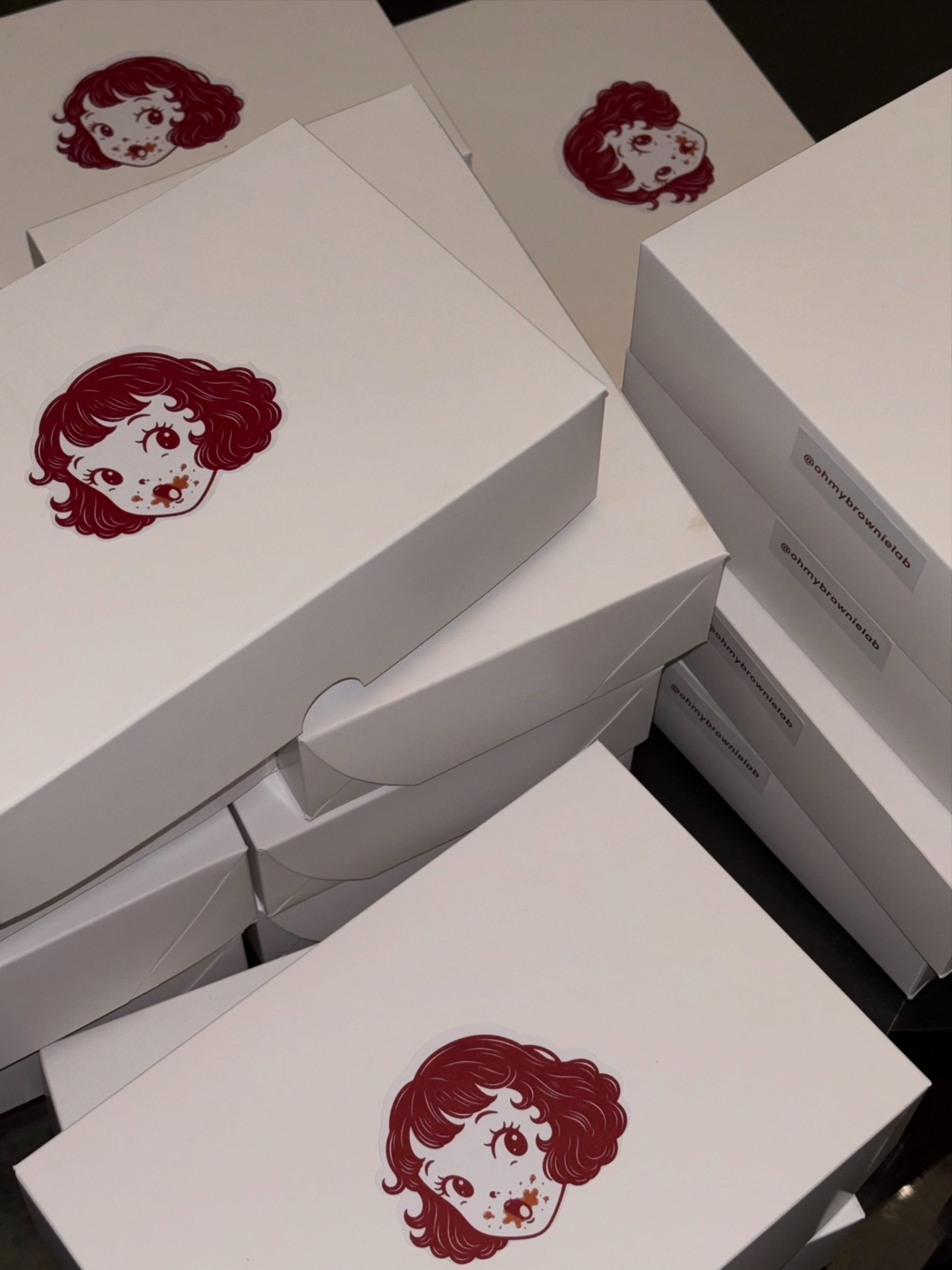 Caixas brancas da Oh My Brownie empilhadas, com a logo estampada